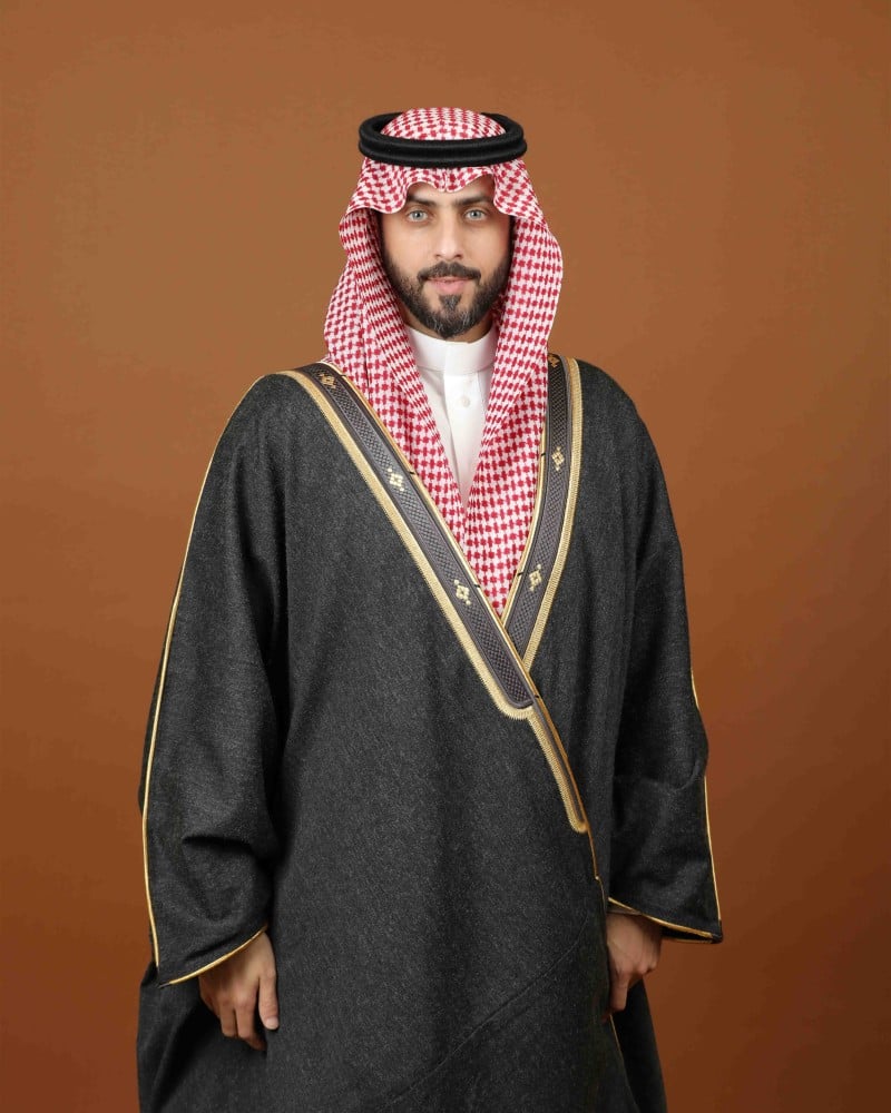 رجل يرتدي مشلحاً شتوياً رمادياً بحواف ذهبية وتطريز حريري مع شماغ أحمر (1 من 2)
